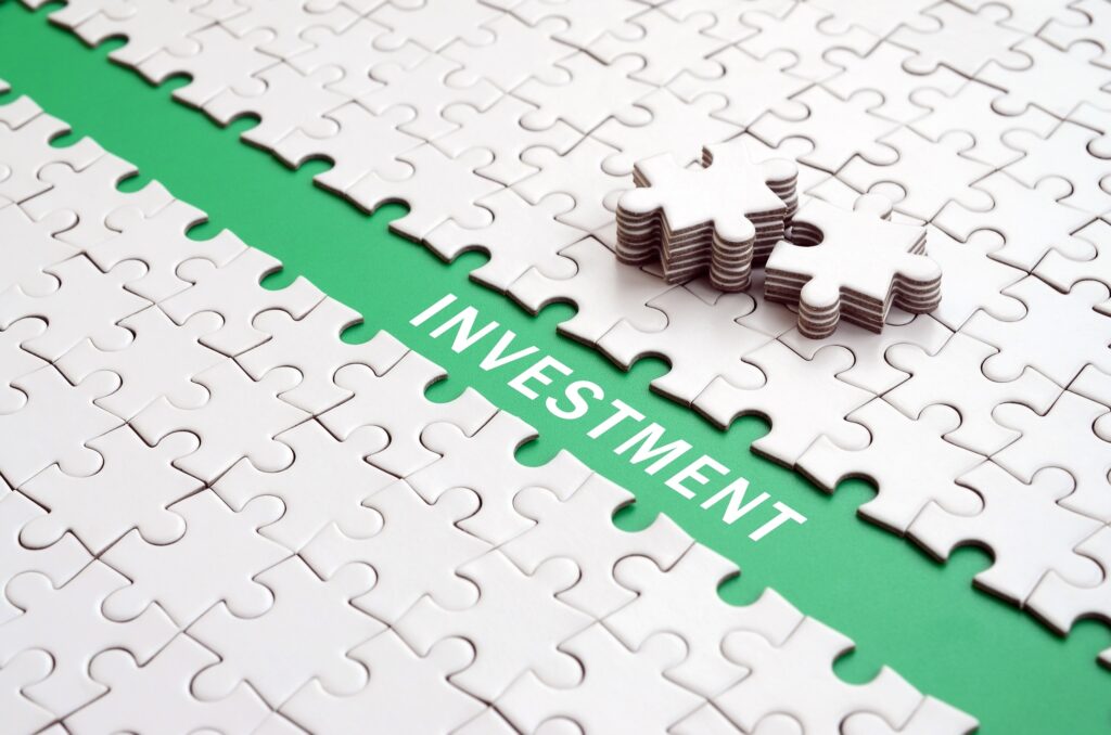 Investment. The green path is laid on the platform of a white folded jigsaw puzzle. The missing elements of the puzzle are stacked nearby
